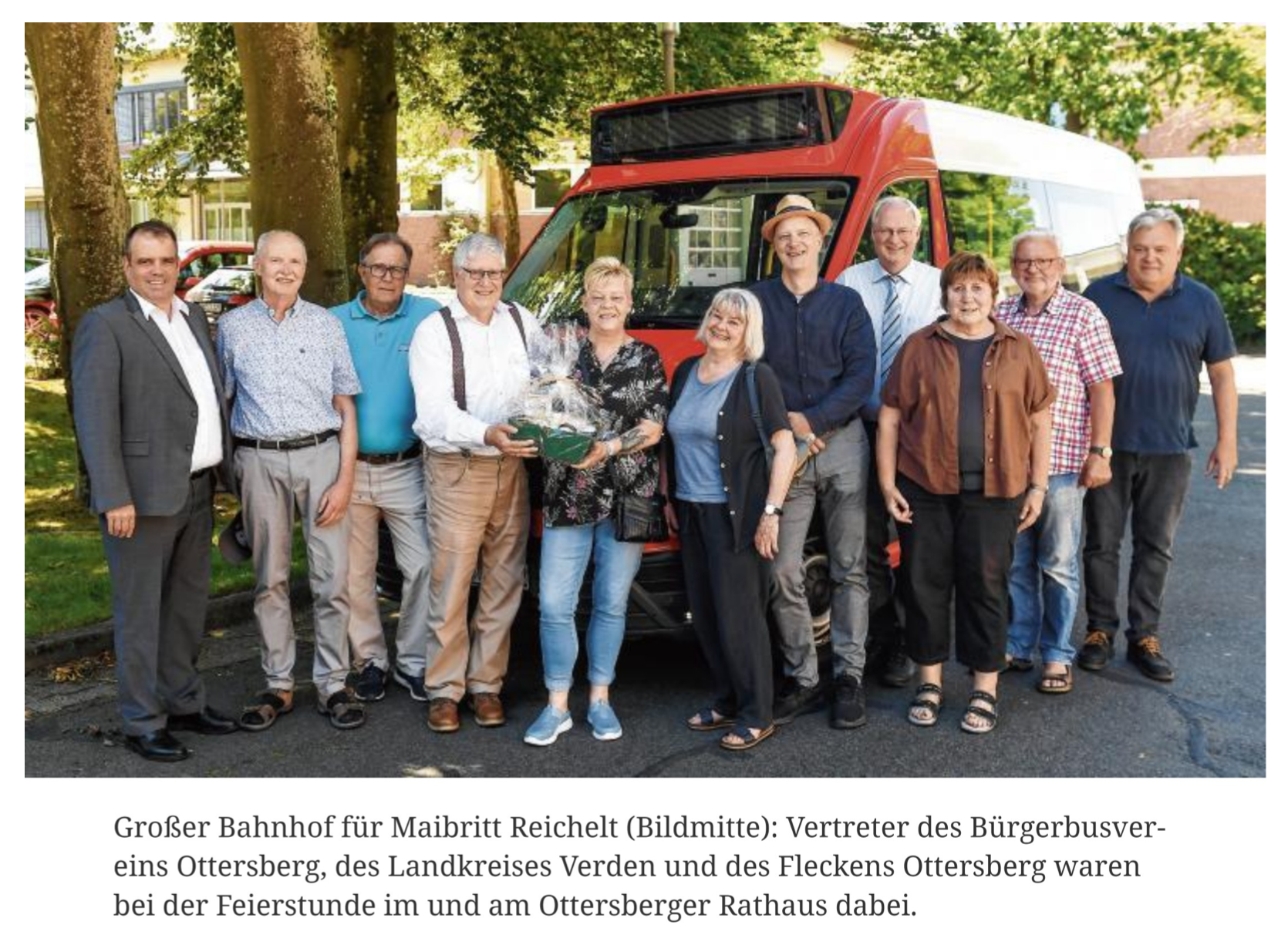 Foto einer Gruppe Menschen vor einem geparkten Bürgerbus. Eine Frau in der Mitte trägt einen Präsentkorb.